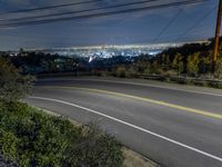 the view from a hill at night, looking down on a roadway and the city below