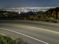 the view from a hill at night, looking down on a roadway and the city below