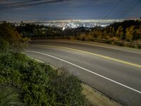 the view from a hill at night, looking down on a roadway and the city below