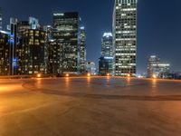 an empty cement parking lot with a city in the distance at night on a rainy night