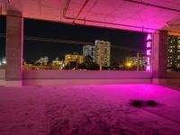 purple lights in an empty building with a view of the city below it at night