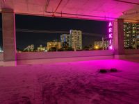 purple lights in an empty building with a view of the city below it at night