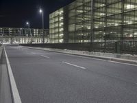 an empty city street at night in front of a large building with a lot of lights on