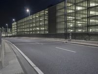 an empty city street at night in front of a large building with a lot of lights on
