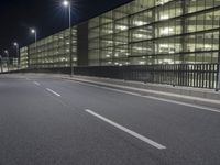 an empty city street at night in front of a large building with a lot of lights on