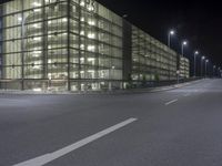 an empty city street at night in front of a large building with a lot of lights on