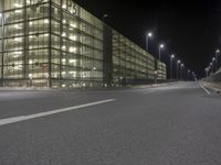 an empty city street at night in front of a large building with a lot of lights on
