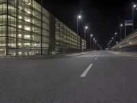 an empty city street at night in front of a large building with a lot of lights on