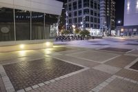 a empty building in a city at night with traffic coming by on a brick plaza