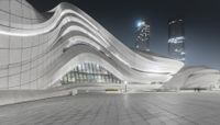 a long curved building has its light on in front of the cityscape at night