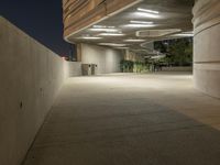 the concrete walkway between two large cement buildings is lit up at night and a man sitting on a bench in the shade, under the street lights of a light