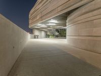 the concrete walkway between two large cement buildings is lit up at night and a man sitting on a bench in the shade, under the street lights of a light