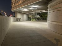 the concrete walkway between two large cement buildings is lit up at night and a man sitting on a bench in the shade, under the street lights of a light