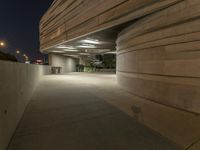 the concrete walkway between two large cement buildings is lit up at night and a man sitting on a bench in the shade, under the street lights of a light