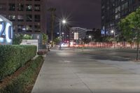 a street sign and sidewalk leading to a business center in the city at night with a light shine