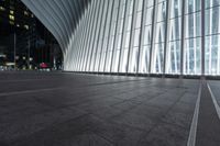 an empty concrete ground and some windows at night in a building with large vertical light panels and black flooring