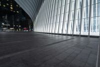 an empty concrete ground and some windows at night in a building with large vertical light panels and black flooring