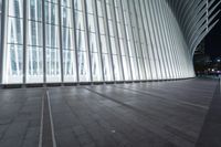 an empty concrete ground and some windows at night in a building with large vertical light panels and black flooring