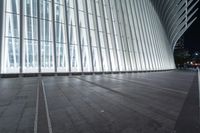 an empty concrete ground and some windows at night in a building with large vertical light panels and black flooring