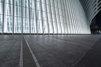 an empty concrete ground and some windows at night in a building with large vertical light panels and black flooring