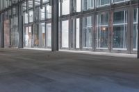 an empty walkway next to windows in an office building where someone is waiting at the door