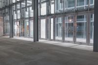 an empty walkway next to windows in an office building where someone is waiting at the door