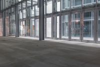 an empty walkway next to windows in an office building where someone is waiting at the door
