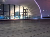 an empty empty sidewalk in front of a large building with lots of glass windows and doors