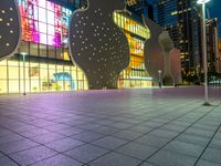 people in front of a large building with windows at night with lights on them and trees in foreground