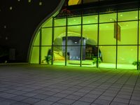 a green lit entrance in front of a building at night a clock is set up outside the entrance