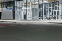 the car is parked on the road outside the large building, at night or in front of some glass doors