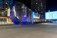 people are walking around by modern architecture at night, some are lights on, in the street