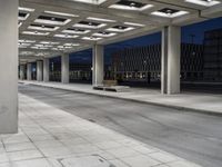 a bench sitting under an overhang at night in a city park area surrounded by concrete columns