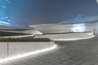 an exterior view of a curved building at night and people on the sidewalk near it