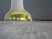 a building with a white facade lit up at night, there is a small area of pavement in the front