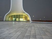 a building with a white facade lit up at night, there is a small area of pavement in the front