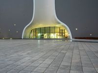 a building with a white facade lit up at night, there is a small area of pavement in the front