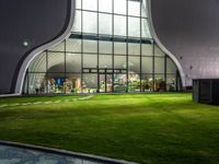 a courtyard area with a grassy lawn area under the glass windows that are lit up