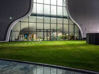 a courtyard area with a grassy lawn area under the glass windows that are lit up