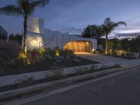 a house at night with lights on the side and palm trees near by in front of the home