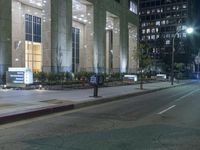 a parking meter on the sidewalk in front of a large building at night with the city lights on