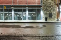 wet asphalt is on the side of an empty street at night with a building in the background