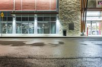 wet asphalt is on the side of an empty street at night with a building in the background