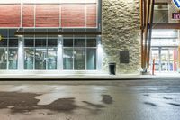 wet asphalt is on the side of an empty street at night with a building in the background