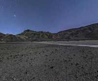 the view of the mountains at night from outside of a desert area, with stars shining brightly