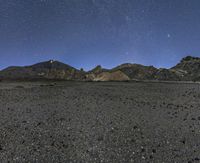 the view of the mountains at night from outside of a desert area, with stars shining brightly