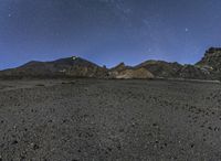 the view of the mountains at night from outside of a desert area, with stars shining brightly