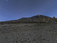 the view of the mountains at night from outside of a desert area, with stars shining brightly