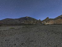 the view of the mountains at night from outside of a desert area, with stars shining brightly