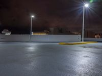 a parking lot at night with lights from above the buildings in the background, a yellow rail line and some blacktop